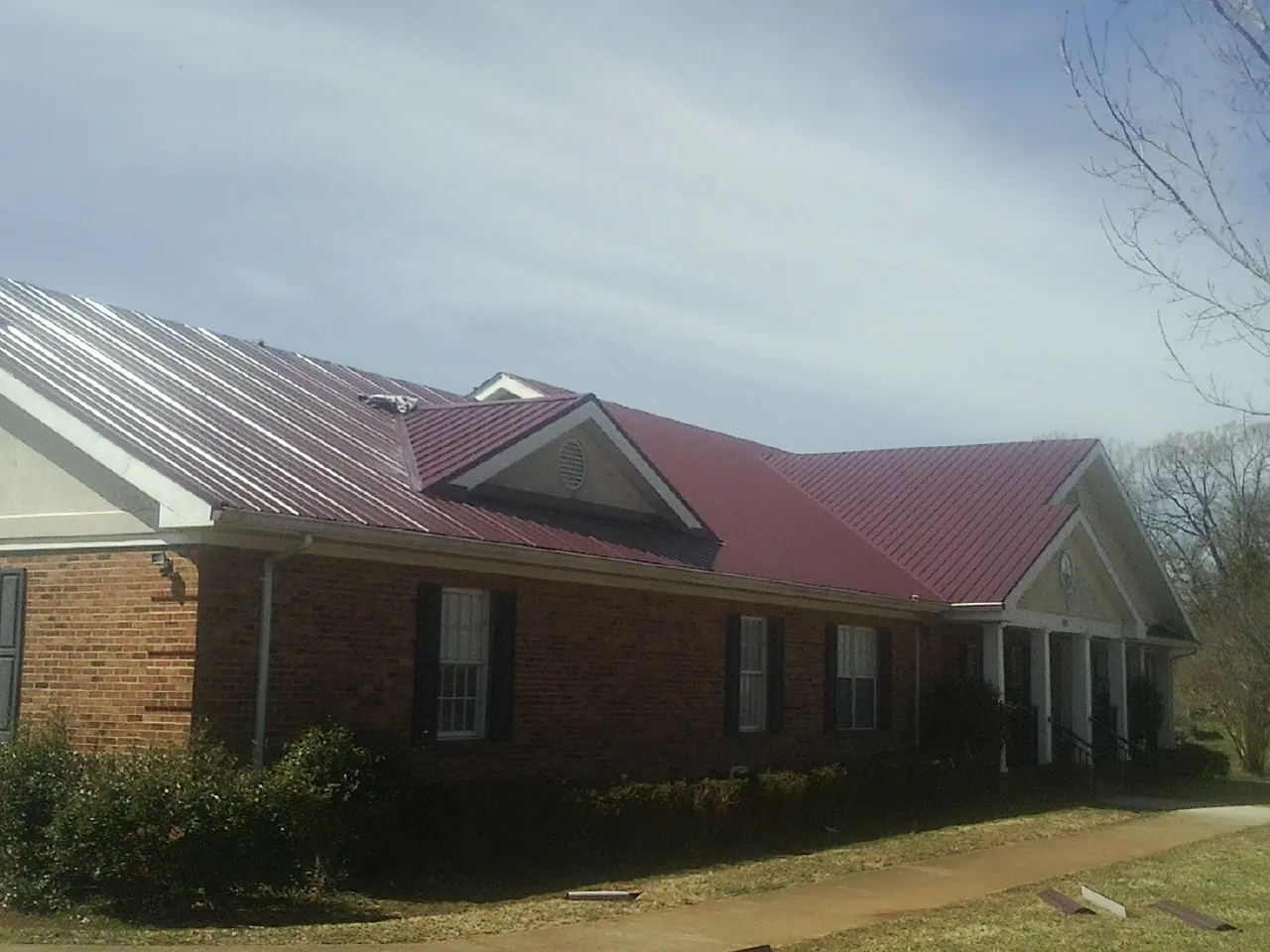 Red metal roof with gabled entries on a long brick building, from a Hail Damage Roof Repair job in Eatonton