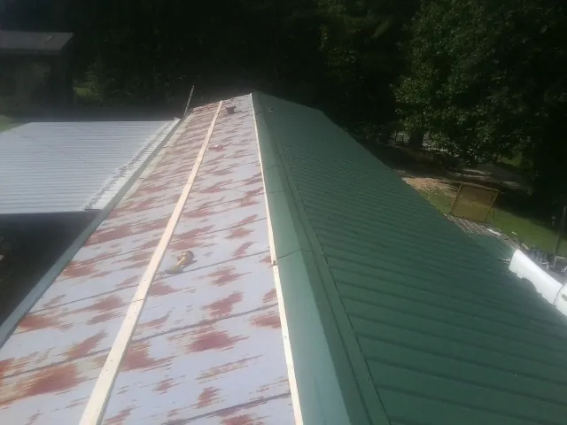 Old rusted panels beside newly installed green metal roofing — Wind Damage Roof Repair by Roofing Brothers in Eatonton