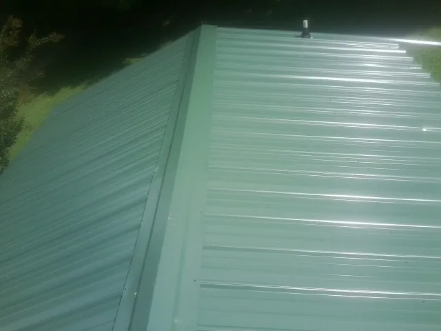 New green metal panels meeting at the ridge of a roof — Flat Roof Repair work by our crew in Eatonton