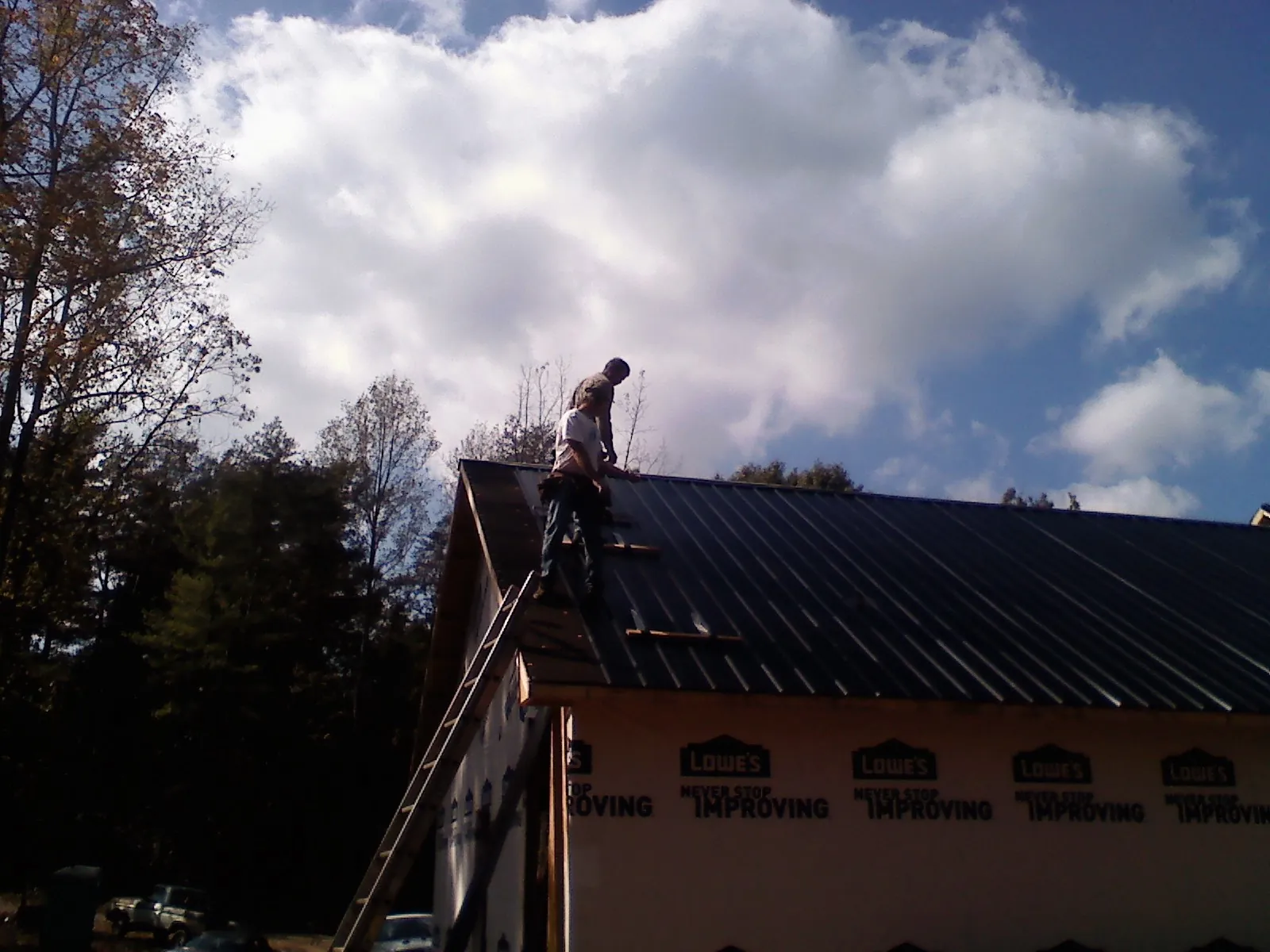 Roofer fastening dark metal panels high against a cloudy sky, from a Roof Inspection job in Eatonton
