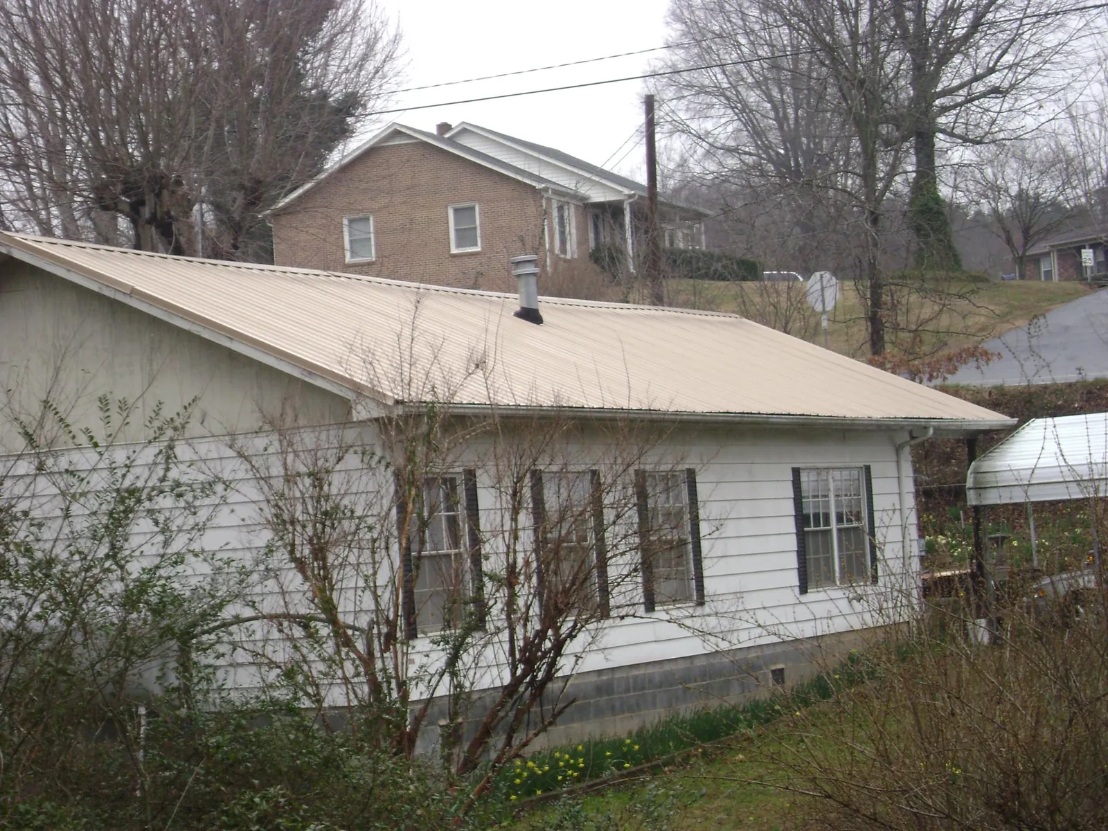 Tan metal roof on a white sided house set into a hillside — Commercial Roofing by Roofing Brothers in Eatonton